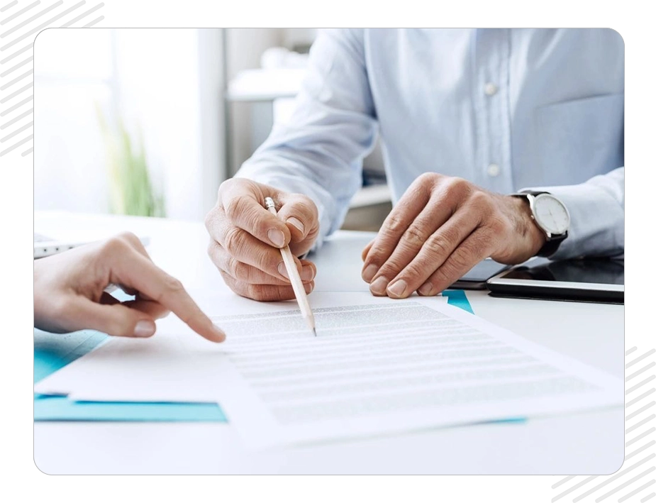 Two people are sitting at a table and one is pointing to the paper.