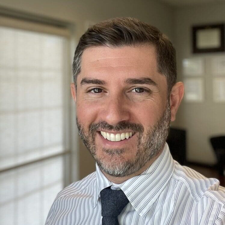 A man in a striped shirt and tie smiling for the camera.